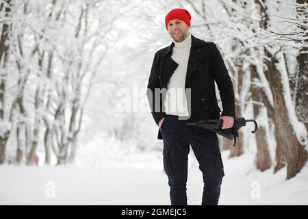 Ein Mann auf einem Spaziergang im Park. Junger Mann mit Regenschirm unter dem Winterschnee. Stockfoto