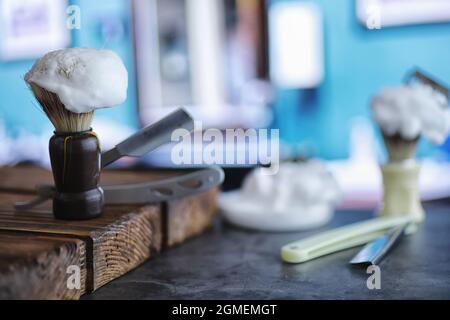 Rasierzubehör auf einem Hintergrund mit Holzstruktur. Werkzeuge. Einweg-Rasierer, Bürste, Rasierer mit Schaumgefahr. Stockfoto