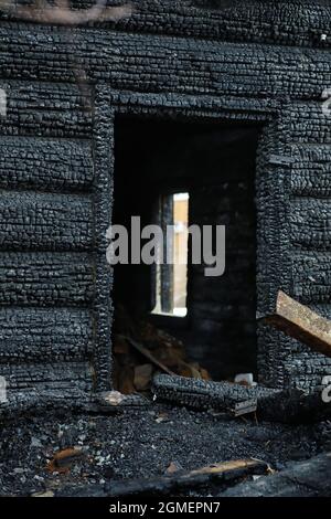 Holzhaus nach dem Feuer. Kohlen auf den Protokollen. Die Asche des Hauses aus dem Feuer. Verbrannte zerstörte Hütte. Stockfoto