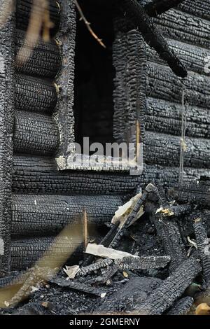 Holzhaus nach dem Feuer. Kohlen auf den Protokollen. Die Asche des Hauses aus dem Feuer. Verbrannte zerstörte Hütte. Stockfoto