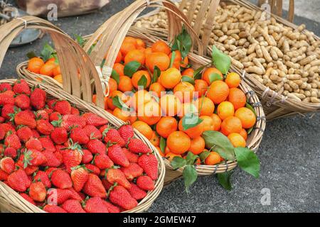 Orangen, Erdbeeren und Erdnüsse in Holzkorb auf dem Markt mit selektivem Fokus Stockfoto