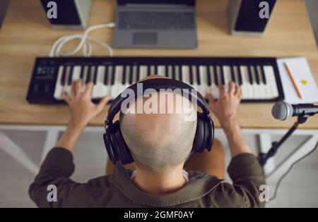 Kahlköpfiger Musiker mit Kopfhörern, der Musik aufnimmt, die er auf dem MIDI-Keyboard spielt Stockfoto