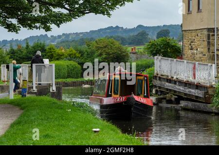 Leute beobachten, wie ein Schmalboot gemietet wird, das an der Micklethwaite Swingbridge vorbeifährt, manuelle Barrieren sind offen - Leeds Liverpool Canal, Yorkshire, England. Stockfoto