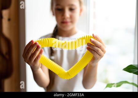 Anti Stress sensorische Pop-Tube Kunststoff-Spielzeug in den Händen eines Kindes. Ein kleines glückliches Kind Mädchen spielt mit einem Poptube Fidget Spielzeug zu Hause. Kinder halten und pla Stockfoto