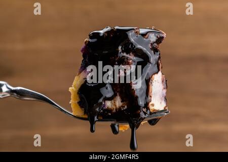 Ein Stück köstlicher hausgemachter Heidelbeere und bröckeliger Käsekuchen, gegossen mit Schokoladensirup auf einer Metallgabel. Stockfoto