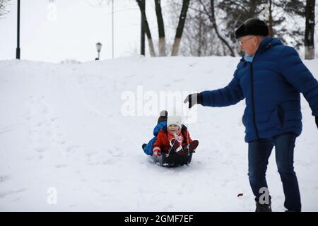 Kinder im Park im Winter. Kinder spielen mit Schnee auf dem Spielplatz. Sie Formen Schneemänner und rutschen Hügel hinunter. Stockfoto