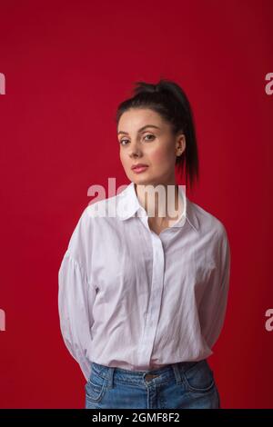 Schöne junge Frau in legerer Kleidung. Studioportrait einer hübschen Frau in den 30er Jahren in weißem Hemd und klassischer blauer Jeans in der Kamera Stockfoto