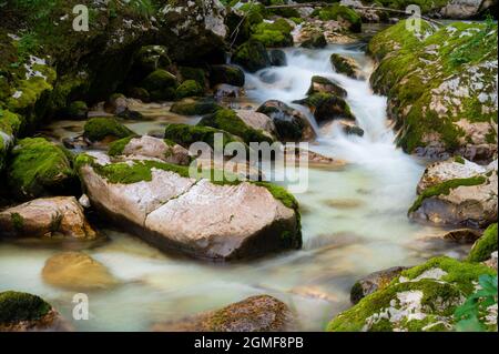 Verschwommenes Bild eines schönen Wasserstroms, der über moosige Felsen in friedlicher Natur fließt. Stockfoto
