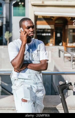 afrikanischer Mann, der auf der Straße in der Nähe eines Rollers steht und telefoniert. Stockfoto