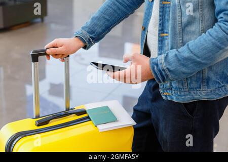 Smartphone in männlicher Hand am Flughafen. Urbane Reisende tragen legere hält Handy. Mann schreibt eine SMS, während er den Koffer im Gepäck hält Stockfoto