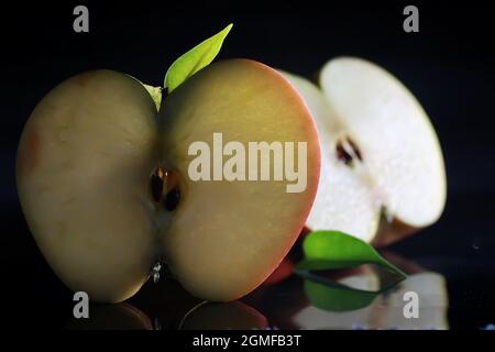 Komposition mit Apfelscheiben auf schwarzem Hintergrund. Eine Apfelscheibe mit Hintergrundbeleuchtung auf schwarzem Hintergrund und Wassertropfen. Saftiger Apfel auf dem Tisch. Stockfoto