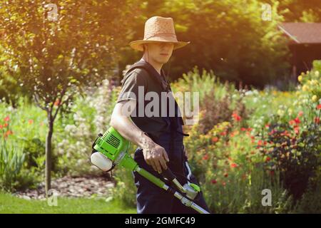 Ein junger Mann mit einem Rasenmäher kümmert sich um das Gras im Hinterhof. Stockfoto