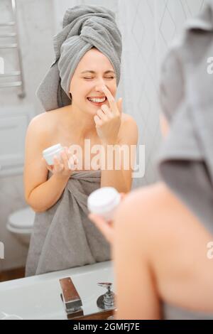Eine junge Frau in grauen Handtüchern im Badezimmer trägt ein Serum auf ihr Gesicht auf. Stockfoto