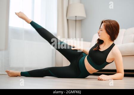 Junge hübsche Frau trainiert zu Hause auf dem Boden mit Yoga. Stockfoto