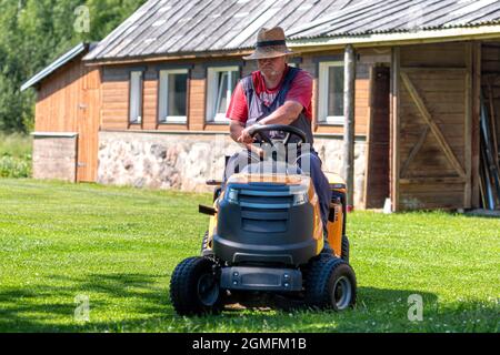 Velena, Lettland - 19. Juni 2021: Ein älterer Mann mit einem Rasenmäher mäht das Gras auf dem Hof des Landhauses Stockfoto