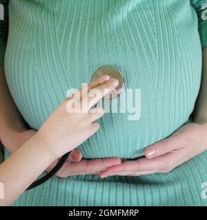 Tochter Arzt mit Stethoskop weiß untersuchen schwangere Mutter. Stockfoto