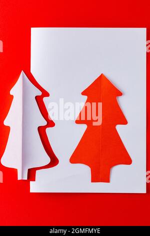 Papier Weihnachtsbaum auf einem roten Hintergrund. Weihnachtsbaum aus weißem Papier. Minimalkonzept Weihnachten Stockfoto