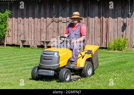Ein älterer Mann mit einem Rasenmäher mäht das Gras im Hof des Landhauses Stockfoto