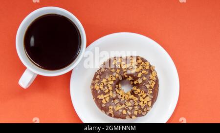 Ein Schokoladendonut und schwarzer Americano-Kaffee ohne Milch in einer weißen Tasse auf hellem Hintergrund. Draufsicht, flach liegend. Frisch gebrüht oder sofort heiß Stockfoto