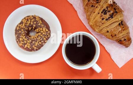 Ein Schokoladendonut, ein Croissant und schwarzer Americano-Kaffee ohne Milch in einer weißen Tasse auf hellem Hintergrund. Draufsicht, flach liegend. Frisch gebraut oder Stockfoto