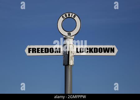 Altes Straßenschild mit Freiheit und Sperre, das in entgegengesetzte Richtungen gegen einen blauen Himmel zeigt. Covid 19-Konzept Stockfoto