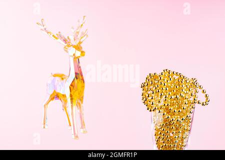 Toy Hirsch und Weihnachtsperlen in einem Champagnerglas auf einem rosa Hintergrund. Weihnachtskomposition mit holographischem Spielzeug Hirsch. Festliches Weihnachtskonzept. Kopieren Stockfoto