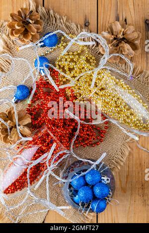 Zwei Sektgläser mit Weihnachtsperlen. Weihnachtskugeln und Dekorationen auf Sacktuch. Tannenzapfen und bunte Perlen auf Holzhintergrund. Oben Stockfoto
