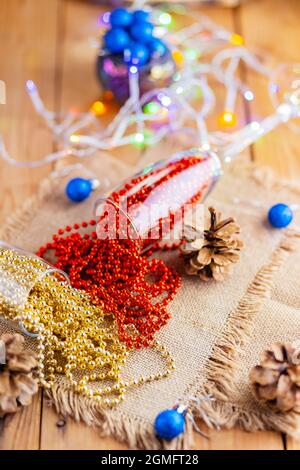 Zwei Sektgläser mit Weihnachtsperlen. Weihnachtskugeln und Dekorationen auf Sacktuch. Tannenzapfen und bunte Perlen auf Holzhintergrund. Oben Stockfoto