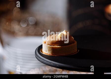 Teig-Tartlet-Nüsse mit Karamell auf schwarzem Tablett, kleines rundes Tartlet mit verschiedenen Füllungen, knuspriges Tartlet mit Haselnüssen, Erdnüssen und anderen eingekochten Stockfoto