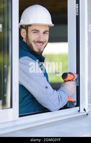 Arbeiter, der Schutzhelm trägt, bohrt Löcher in ein Fenster Stockfoto