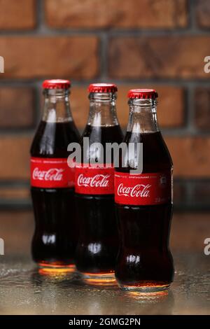 RIVNE, UKRAINE JUNI 26 2020: Drei klassische Glasflaschen von Coca-Cola auf Backsteinwand. Dosen von Coca-Cola. Stockfoto