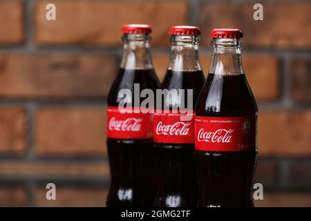 RIVNE, UKRAINE JUNI 26 2020: Drei klassische Glasflaschen von Coca-Cola auf Backsteinwand. Dosen von Coca-Cola. Stockfoto