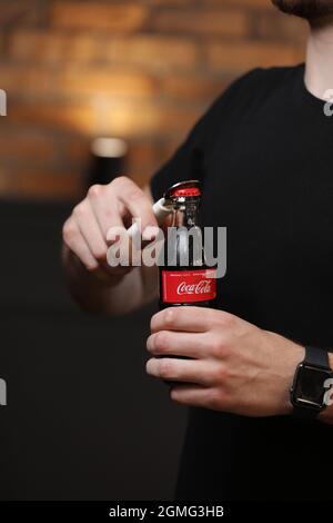 RIVNE, UKRAINE JUNI 26 2020: Ein junger Mann öffnet eine Glasflasche Coca-Cola mit Flaschenöffner. Stockfoto