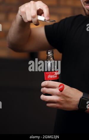 RIVNE, UKRAINE JUNI 26 2020: Ein junger Mann öffnet eine Glasflasche Coca-Cola mit Flaschenöffner. Stockfoto