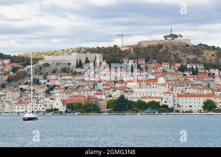 Sibenik, Kroatien - 25. August 2021: Altes Haus mit Hafen, Promenade, Steinhäusern, Kathedrale und Festung, die vom Meer aus gesehen wird, wenn man mit dem Schiff ankommt Stockfoto