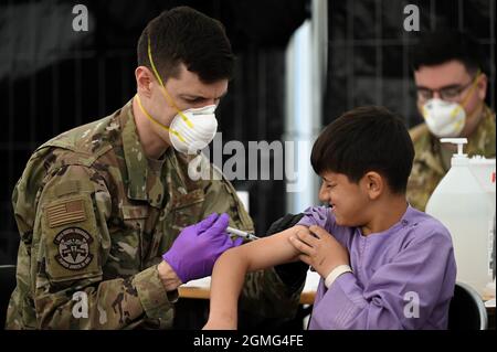 Ramstein-Miesenbach, Deutschland. September 2021. Ein US-Luftwaffenflieger verabreicht einem afghanischen Kind, das am 18. September 2021 auf dem Luftwaffenstützpunkt Ramstein in Ramstein-Miesenbach aus Kabul evakuiert wurde, Impfstoffe gegen Mumps, Masern und Röteln sowie Windpocken. Ramstein bietet im Rahmen der Operation Allies Refuge eine vorübergehende Unterkunft für Evakuierte aus Afghanistan an. Kredit: TSgt. Devin Nothstine/USA Air Force/Alamy Live News Stockfoto