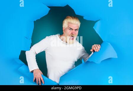 Schockierter Mann, der durch das Loch schaut. Überraschte Bartender, der ein Loch in Papier machte. Rabatt, Verkauf, Saisonverkauf. Stockfoto