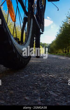 Fahrradräder fahren auf einer asphaltierten Straße vor dem Hintergrund des blauen, hellen Himmels. Unscharf, verschwommen, von unten, von der Straße fotografiert Stockfoto