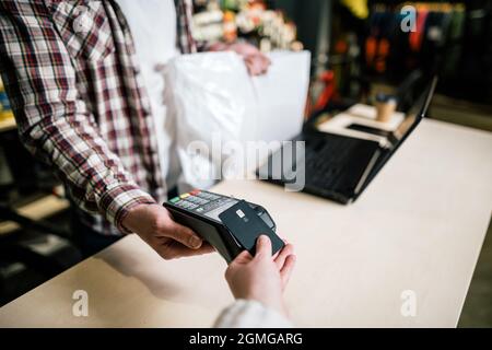 Close-up Shopper Hand gibt Kreditkarte über Zahlungsterminal zu zahlen, Verkäufer hinter dem Schalter macht die Zahlung und gibt Waren in Box an den Käufer. Nutzung bezahlen Stockfoto