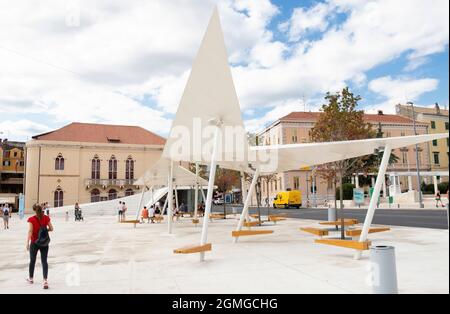 Sibenik, Kroatien - 25. August 2021: Stadtplatz Poljana mit Baldachin Bänken und Freilufttribünen, und Theatergebäude dahinter Stockfoto