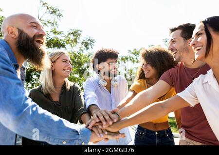 Eine Gruppe von vereinten, multirassischen Menschen, die die Hände zusammenstapeln - multiethnische junge Studenten, die gemeinsam an der Universität auf dem Campus feiern Stockfoto