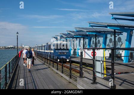 Der Pier-Zug fährt von der Pier-Endstation am Southend Pier ab, wobei Wanderer an einem sonnigen Septembertag zurücklaufen. Besucher auf dem Rückweg zum Ufer Stockfoto