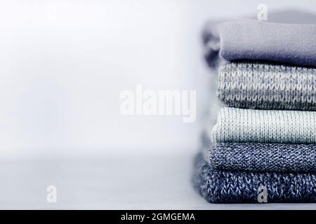 Stapel gestrickter Pullover und Pullover auf grauem, unscharfem Beton-Hintergrund. Speicherplatz kopieren Stockfoto