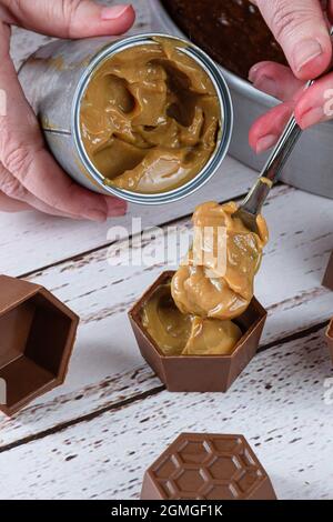 Konditor setzt einen Löffel Dulce de leche in kleine Schokoladenformen, um brasilianischen Honigkuchen zu machen. Stockfoto