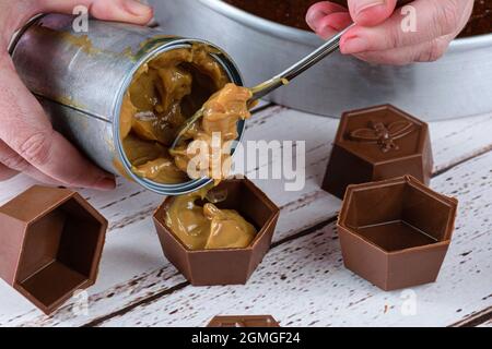 Nahaufnahme des Konditoreiers, der einen Löffel Dulce de leche in kleine Schokoladenformen legt, um brasilianischen Honigkuchen zu machen. Stockfoto