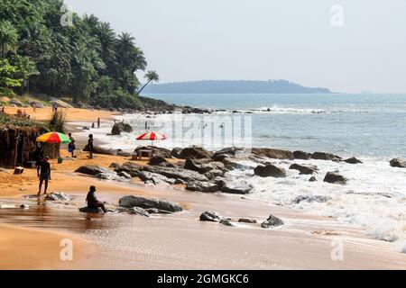 Menschen am Sandstrand mit einigen großen Felsen an einem sonnigen Tag auf einer Insel vor der Küste von Guinea, Westafrika. Stockfoto