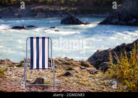 Klappstühle am Ufer eines Bergflusses an einem schönen, warmen Tag. Ein ruhiger und ruhiger Ort zum Entspannen und Nachdenken. Ausrüstung und die Erholung des Touristen. Stockfoto