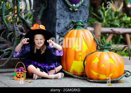 Kind im Halloween Kostüm. Kinder können sich verwöhnen lassen. Kleines Mädchen als Hexe gekleidet mit Hut hält Kürbis Laterne und Süßigkeiten Eimer. Feier. Stockfoto