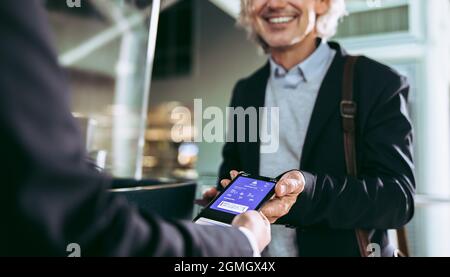 Ausschnittene Aufnahme eines männlichen Passagiers, der mit einem digitalen Flugticket am Flughafenterminal eingecheckt hat. Geschäftsmann zeigt den Mitarbeitern die Bordkarte des Flugzeugs auf dem Handy Stockfoto