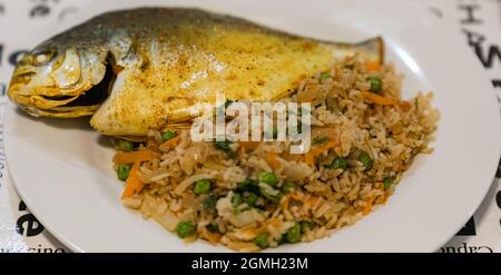 Gebratener Fisch mit Reis und Gemüse auf einem Teller. Hausmannskost Stockfoto